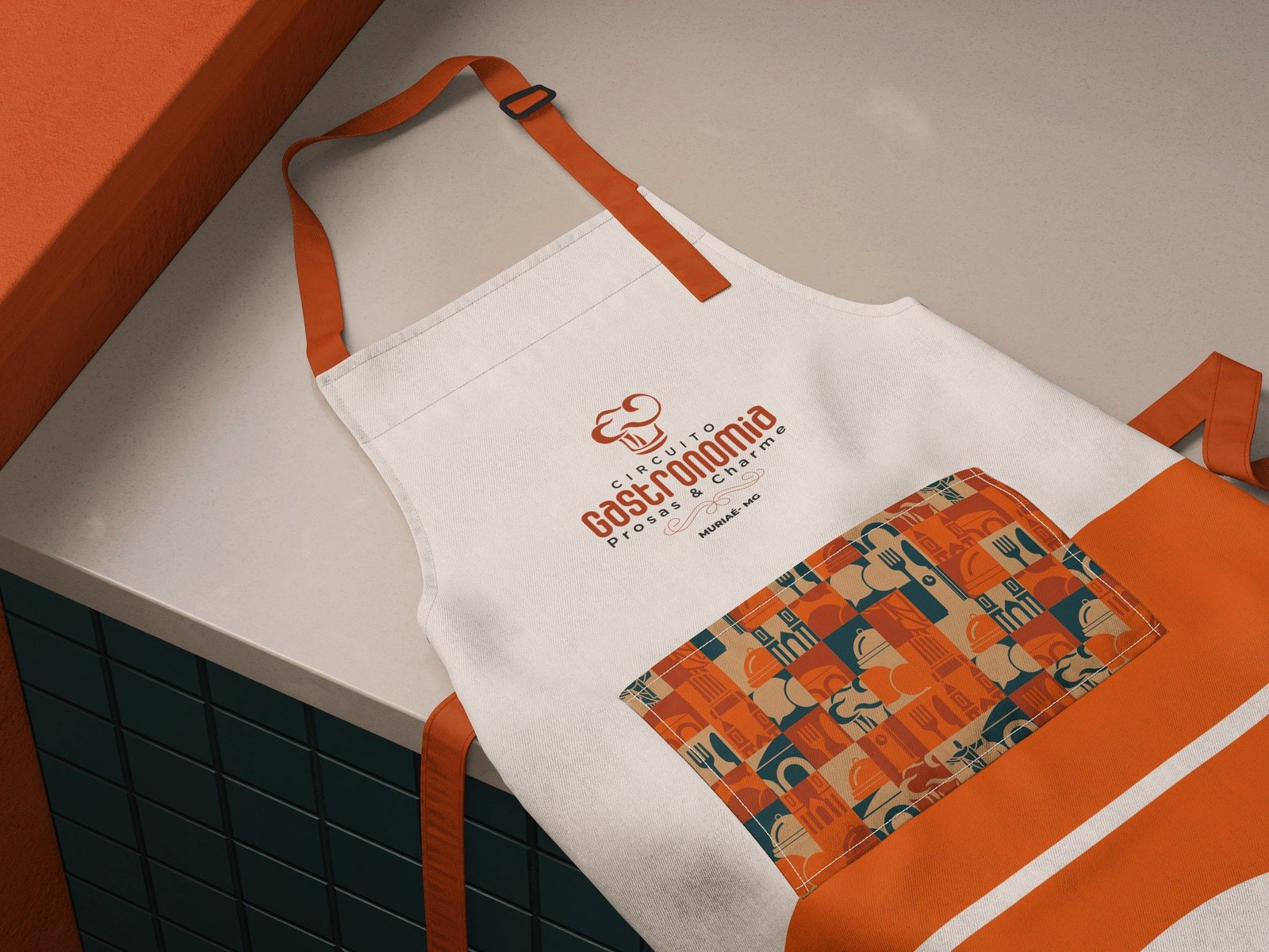 Avental claro com o logo do circuito e um bolso estampado com os ladrilhos da identidade.
